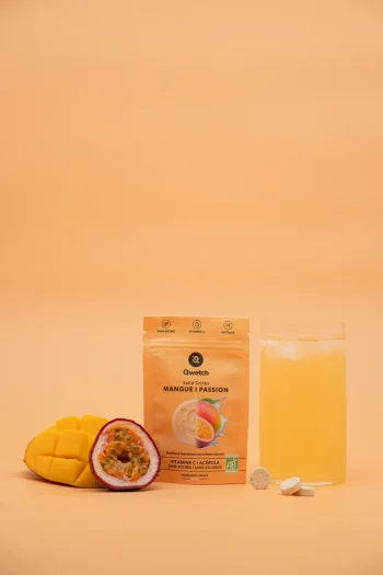 Embalagem de Solid Drink Bio sabor manga e maracujá da Qwetch com fruta fresca, copo com bebida e duas pastilhas brancas. Compra já online!