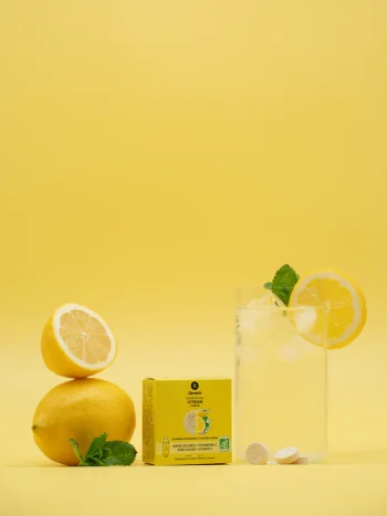 Embalagem amarela de Solid Drink Bio sabor limão da Qwetch com limões frescos, folhas de hortelã e duas pastilhas em destaque.