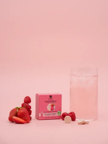 Embalagem rosa de 3 pastilhas Solid Drink Bio sabor morango e framboesa da Qwetch com frutas frescas, copo com bebida rosa e pastilhas ao lado.