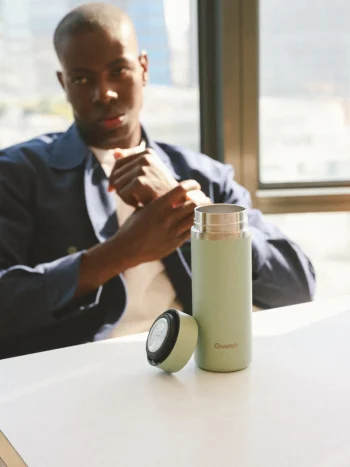 Garrafa térmica Qwetch de 400ml na cor verde tília, com tampa ao lado, sobre mesa em ambiente interior com luz natural.