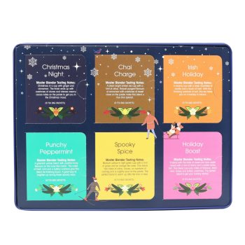 Lata azul Premium Holiday Collection da English Tea Shop aberta, mostrando seis compartimentos coloridos com diferentes blends de chá biológico: Christmas Night, Chai Charge, Irish Holiday, Punchy Peppermint, Spooky Spice e Holiday Boost.